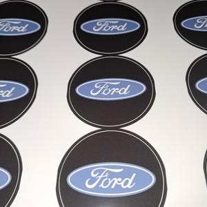Könnte beinhalten: Mehrere schwarz-weiße Ford-Logo-Aufkleber. Jeder Aufkleber hat einen schwarzen Hintergrund mit weißem Rand und ein hellblaues Oval mit dem Wort "Ford" in weißer Schrift. Die Aufkleber sind in einem Raster angeordnet.