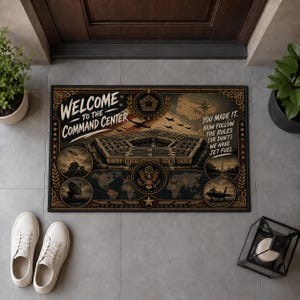 May include: A rectangular doormat featuring a graphic of the Pentagon building, a world map, and military imagery. Text reads: WELCOME TO THE COMMAND CENTER. YOU MADE IT. NOW FOLLOW THE RULES (OR DON'T) WE HAVE JET FUEL. The design includes gold and black tones.