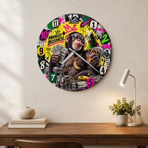 Könnte beinhalten: Eine runde Wanduhr mit einem lebendigen Graffiti-Design, das einen Schimpansen mit Sonnenbrille und Goldkette zeigt, der einen Fächer aus Geldscheinen und ein Glas Whiskey hält. Das Zifferblatt enthält den Text Monkey Business und die Zahlen eins bis zwölf.