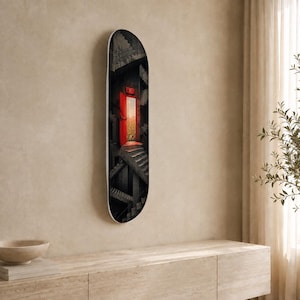May include: A skateboard deck featuring a graphic print of a dark, concrete stairwell with a bright red door slightly ajar. The door reveals a glowing, warm light and a glimpse of greenery inside, with a red sign above the door frame reading EXIT.