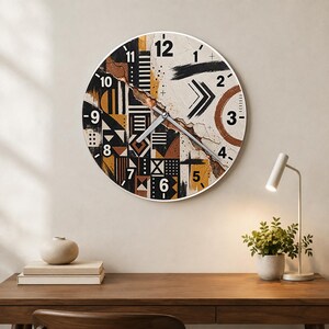 May include: A round wall clock featuring a textured, abstract design in black, white, and shades of brown. The face displays bold black numerals from 1 to 12, geometric patterns, and a central crack-like detail with silver-toned clock hands.