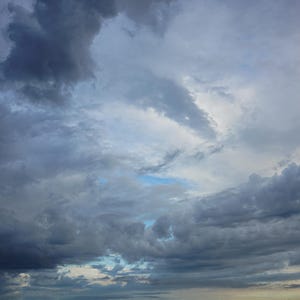 May include: A moody sky dominated by dark, swirling storm clouds. The image presents a palette of grey tones, from deep charcoal to lighter shades, with glimpses of blue. The clouds have a textured, layered appearance, suggesting an impending storm.
