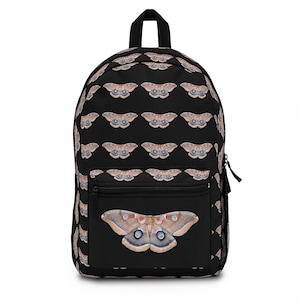 May include: Black backpack featuring a repeating pattern of brown and cream-colored moths. The front pocket showcases a large moth with blue eye-like markings. The backpack has a black zipper and a top handle.