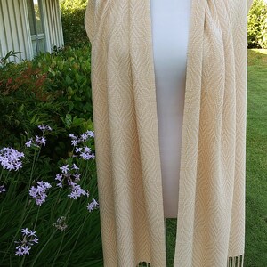 May include: A cream-colored woven scarf with a subtle geometric pattern and fringe tassels.