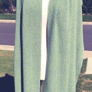 May include: A green and white woven shawl with a fringe border. The shawl is draped over a mannequin.