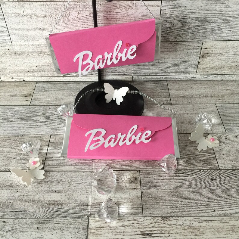 May include: Two pink cardboard boxes with the word "Barbie" printed in white on them. The boxes are decorated with white butterflies and pink rhinestones.