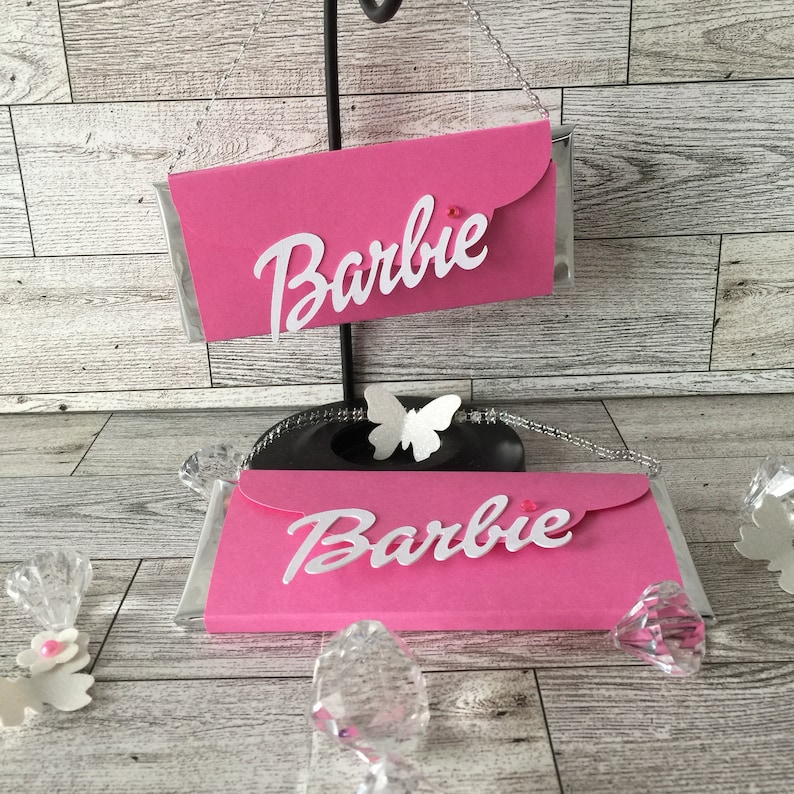 May include: Two pink chocolate bar wrappers with a white butterfly design and the word "Barbie" in white letters.
