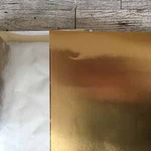 May include: A sheet of silver foil paper next to a sheet of gold foil paper.