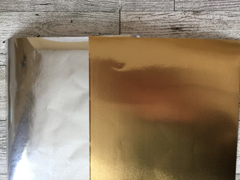 May include: A sheet of silver foil paper next to a sheet of gold foil paper.