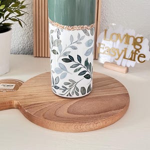 Puede incluir: Una taza de cerámica blanca con un asa negra y el texto "But First, Coffee" en negro y negrita. La taza está sobre una superficie blanca. La taza mide aproximadamente 10 cm de alto.