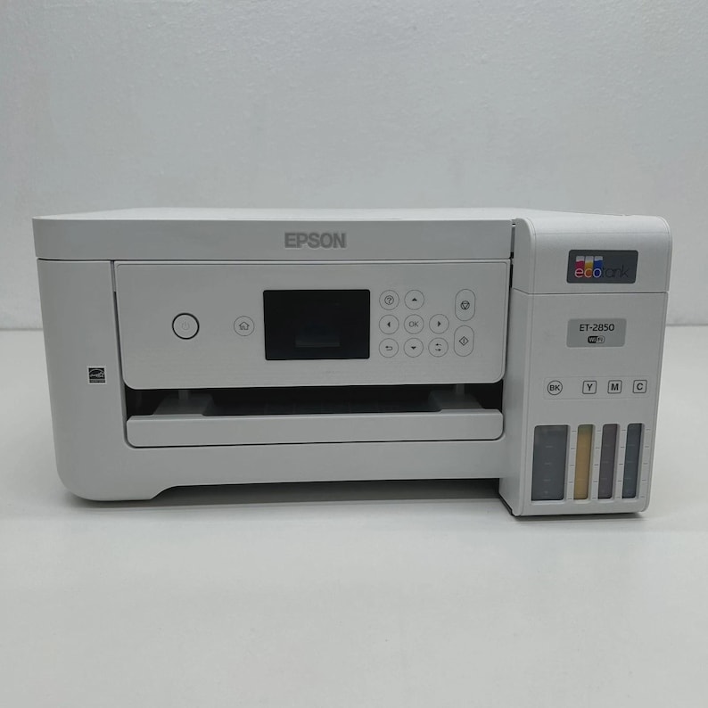 May include: A white Epson ET-2850 all-in-one printer. The printer features a small display screen, control buttons, and ink tanks. The Epson logo is visible on the top. The printer is on a white surface.