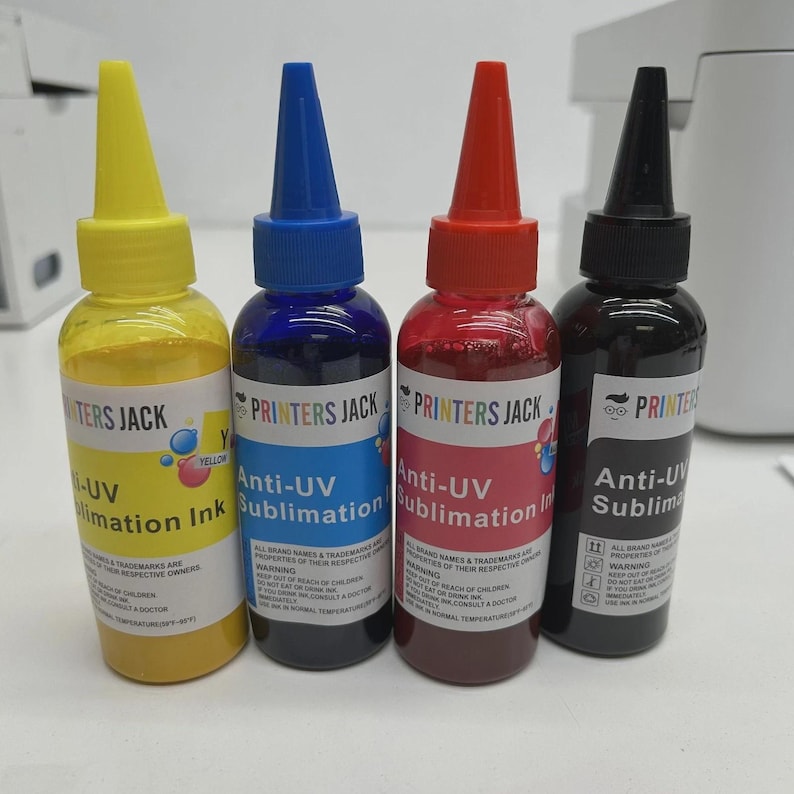 May include: Four bottles of Printers Jack Anti-UV Sublimation Ink in yellow, blue, red, and black. Each bottle has a coloured cap and a label with product information. The bottles are for sublimation printing.