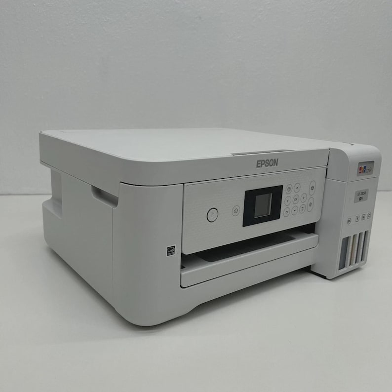 May include: A white Epson printer with a flat top and a control panel featuring a small screen and several buttons. The printer has a paper tray and ink cartridge access. The Epson logo is visible on the top.