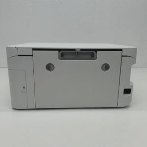 May include: A white printer with a flat top and a grey handle. The printer has a rectangular shape with rounded corners and a small power button on the side. The printer is designed for home or office use.
