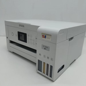 May include: A white Epson ET-2850 all-in-one printer. The printer has a flat top and a control panel with buttons and a small screen. The ink tanks are visible on the side. The printer has the "EcoTank" logo.