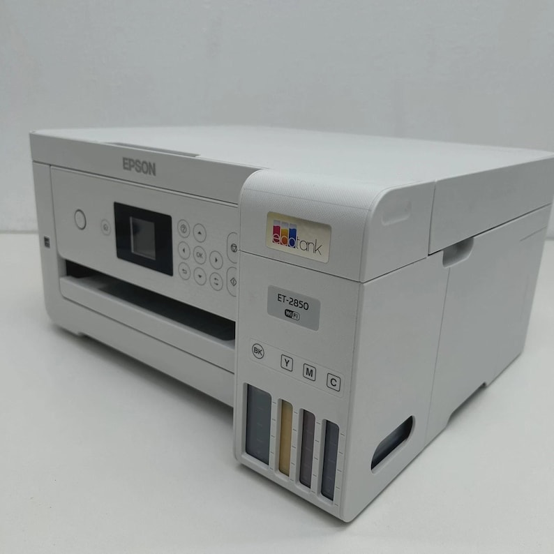 May include: A white Epson ET-2850 all-in-one printer. The printer has a flat top and a control panel with buttons and a small screen. The ink tanks are visible on the side. The printer has the "EcoTank" logo.