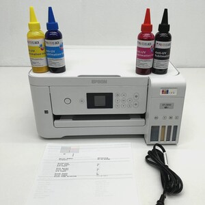 May include: A white Epson ET-2850 printer with four ink bottles in yellow, blue, red, and black. The ink bottles are labelled "Anti-UV Sublimation Ink". A printed sheet of paper and a black power cable are also present.