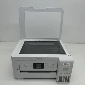 May include: A white Epson ET-2850 all-in-one printer with the top cover open. The printer has a flatbed scanner, control panel, and ink tanks. The Epson logo is visible on the front.