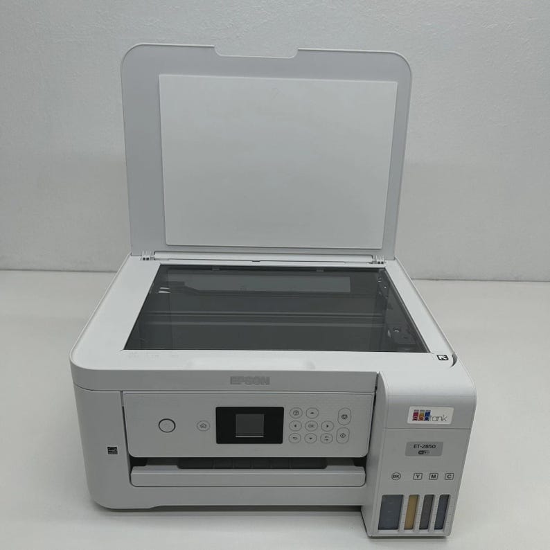 May include: A white Epson ET-2850 all-in-one printer with the top cover open. The printer has a flatbed scanner, control panel, and ink tanks. The Epson logo is visible on the front.