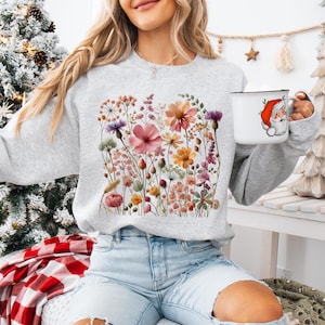 Könnte beinhalten: Ein graues Sweatshirt mit einem Blumendruck mit rosa, gelben und weißen Blumen. Die Blumen sind in einer Gruppe angeordnet und von grünen Blättern umgeben.