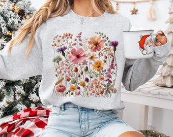 May include: A gray sweatshirt with a floral print featuring pink, yellow, and white flowers. The flowers are arranged in a cluster and are surrounded by green leaves.