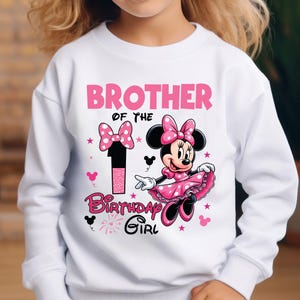 May include: White sweatshirt with a pink Minnie Mouse graphic. The design includes the text "BROTHER OF THE BIRTHDAY GIRL" and the number "1". Minnie Mouse is wearing a pink dress and bow. The design also features pink stars and bows.