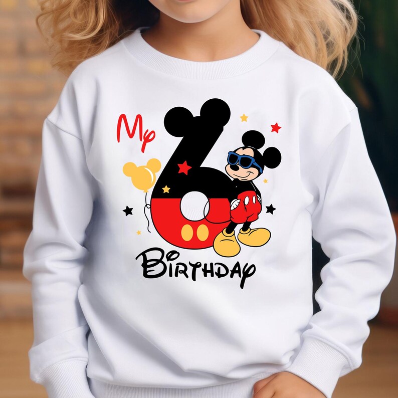 May include: White sweatshirt featuring a colorful Mickey Mouse-themed design. The design includes the number 6, the words "My Birthday", and Mickey Mouse wearing sunglasses. The number 6 is red and black with yellow accents.
