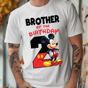May include: White t-shirt with the text "BROTHER OF THE BIRTHDAY" in black and red. A cartoon Mickey Mouse graphic is on the shirt, along with the number 2 in red and black, and the word "BOY" in yellow.