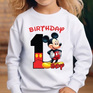 May include: White sweatshirt featuring a Mickey Mouse design for a first birthday. The design includes a large black number 1 with red and yellow accents, the word "BIRTHDAY" in red, and the word "BOY" in yellow.