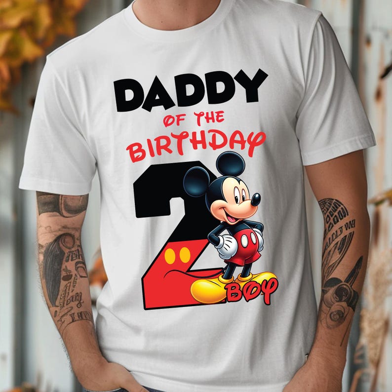 May include: White t-shirt with the text "DADDY OF THE BIRTHDAY BOY" in black and red. A graphic of Mickey Mouse is featured, along with the number 2 in black and red. The design is likely for a birthday celebration.
