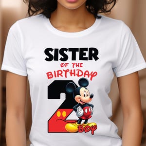 May include: White t-shirt featuring the text "SISTER OF THE BIRTHDAY BOY" in black and red. A large number 2 is designed with a black background and red outline, with Mickey Mouse in the center. The word "BOY" is in yellow.