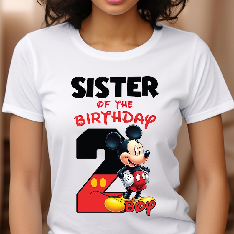 May include: White t-shirt featuring the text "SISTER OF THE BIRTHDAY BOY" in black and red. A large number 2 is designed with a black background and red outline, with Mickey Mouse in the center. The word "BOY" is in yellow.