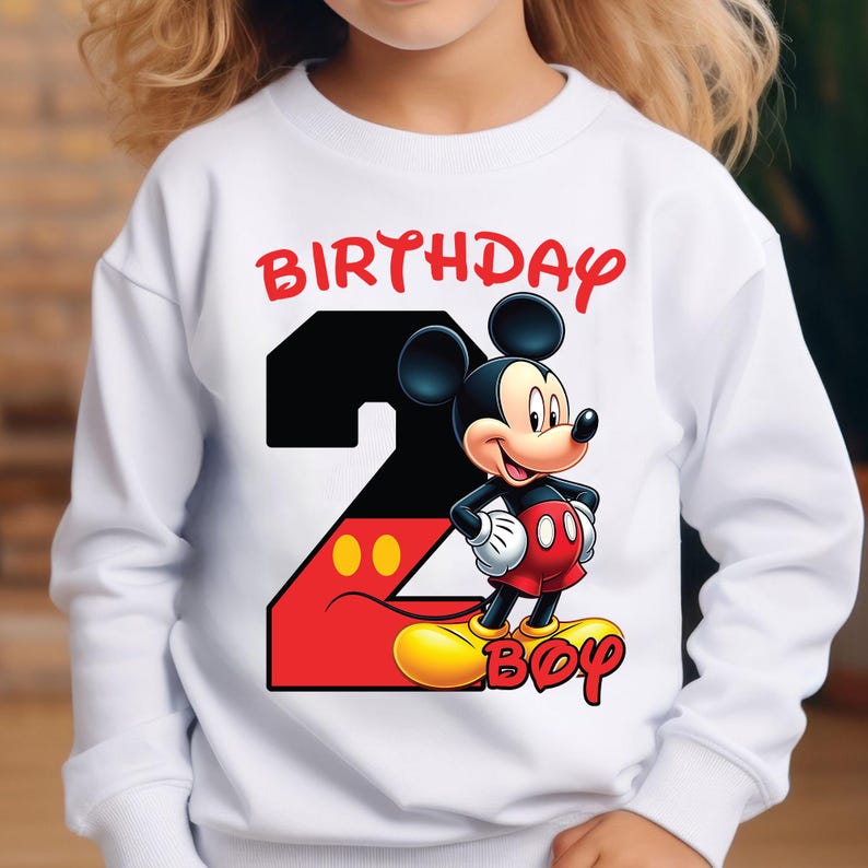 May include: White sweatshirt featuring a colorful graphic of Mickey Mouse, the number 2, and the words "BIRTHDAY BOY" in red. The design includes Mickey Mouse in his classic outfit, with a black and red number 2.