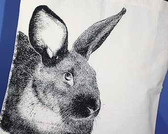 May include: A white canvas tote bag with a black and white illustration of a rabbit's head. The rabbit has large ears and a fluffy appearance.