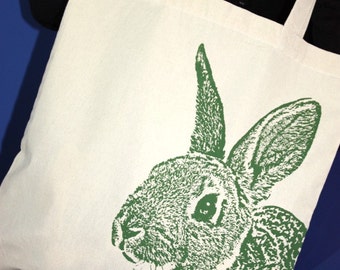 May include: A white canvas tote bag with green rabbit silhouette printed on the front. The rabbit is facing left and has a detailed design.