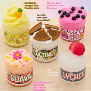 May include: Five colorful jars of scented slime. The jars are labeled "Pineapple Whip", "Coconut", "Passion Fruit", "Guava", and "Lychee". Each jar is decorated with toppings and charms that match the scent, such as a pineapple, flower, and black beads.