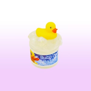 May include: A small, clear container of bubble bath with a yellow rubber ducky on top. The container has a blue label with the words "Bubble Bath" and a picture of a duck. The background is a gradient of purple and white.
