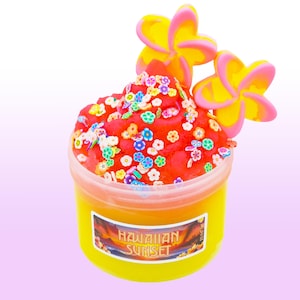 May include: A container of yellow slime with a red topping, decorated with colorful flower-shaped sprinkles. Two yellow and pink plumeria flowers are placed on top. The container has a label that reads "Hawaiian Sunset".
