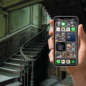 May include: A smartphone with a dark background and a variety of app icons on the screen. The icons include a clock, a calendar, a weather app, and a messaging app. The phone is being held in a hand in front of a dark, old staircase.