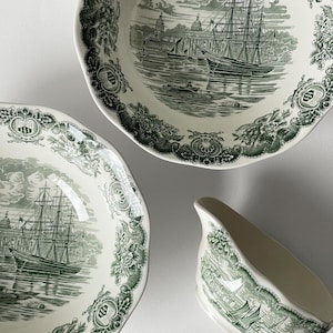 Puede incluir: Un juego de vajilla de cerámica blanca y verde antigua. El juego incluye dos platos y una salsera, todos con una detallada escena náutica con un velero y bordes florales decorativos. Los platos tienen bordes festoneados.