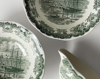 May include: A set of antique white and green ceramic tableware. The set includes two plates and a gravy boat, all featuring a detailed nautical scene with a sailing ship and decorative floral borders. The plates have scalloped edges.