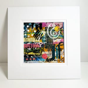May include: Abstract mixed media artwork in a white mat. The artwork features a collage of colors including pink, yellow, blue, and black. White script and a spiral design are layered over the colorful background. The artwork is signed in the lower right corner.