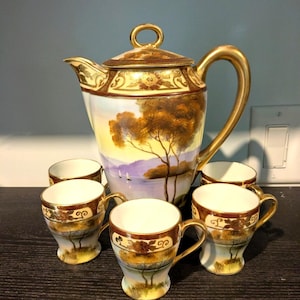 Może przedstawiać: Zestaw do herbaty w stylu vintage z Japonii z pozłacanymi zdobieniami i ręcznie malowanym krajobrazem. Zestaw zawiera czajnik i sześć filiżanek.