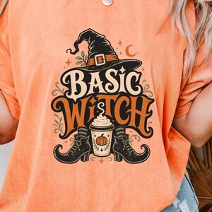 May include: An orange mineral-wash t-shirt featuring a graphic print of a witch hat, a coffee cup with a pumpkin icon, and black boots. The text "BASIC WITCH" is printed in a stylized font above the coffee cup, surrounded by small stars and leaves.