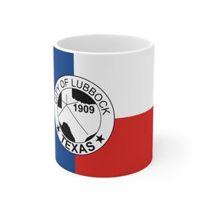 Puede incluir: Una taza de cerámica blanca con la bandera de Texas, que presenta una franja vertical azul a la izquierda y franjas horizontales blanca y roja a la derecha. El sello circular de la ciudad de Lubbock, Texas, 1909 está impreso en negro.
