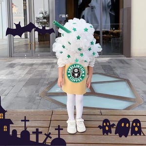 May include: A child's Halloween costume designed to look like a coffee drink. The costume includes a white, fluffy top with green star details, a yellow skirt with a "SKELLINGTON COFFEE" logo, and a green straw. The child wears white tights and shoes.