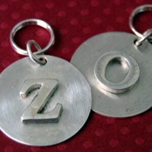 May include: Two silver keychains with round metal tags. One tag has the letter "Z" embossed on it, and the other tag has the letter "O" embossed on it.