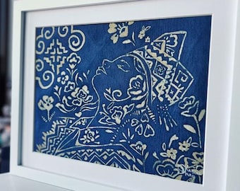 May include: A framed art print featuring a profile of a person with floral and geometric designs in white against a dark blue background. The artwork is in a white frame, creating a clean, modern aesthetic. The print's style suggests a cultural or folk art theme.