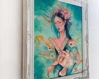 May include: A framed artwork featuring a woman with floral headwear and a tiger cub. The painting has a teal and gold color scheme, with a white ornate frame. The artwork is mounted on a white wall.