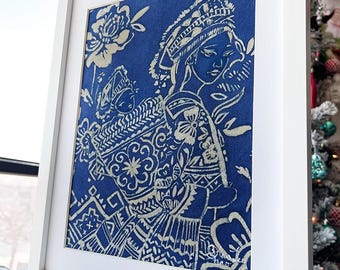 May include: A framed art print featuring a blue background with a cream-colored illustration of figures and floral patterns. The artwork is encased in a white rectangular frame, creating a clean and modern aesthetic.